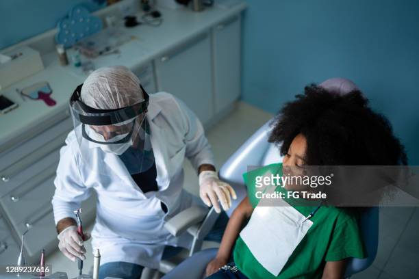 zahnarzt untersucht zähne von kind sitzen im zahnarztstuhl - face shield stock-fotos und bilder