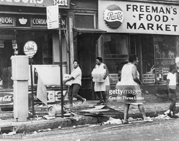 Women carrying boxes along the debris-strewn sidewalk, passing Freeman's Food Market, as looting continued during the riots in Newark, New Jersey,...