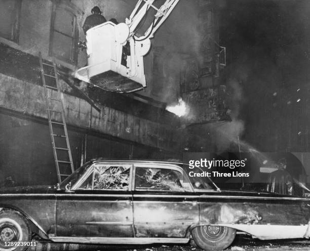 Firefighters in a cherrypicker tackle a fire in a store, above a car which the driver abandoned during a night of rioting in Detroit, Michigan, July...