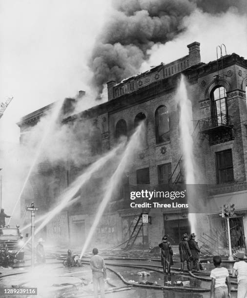 Firefighters extinguish the fire in a burning apartment block set alight after a night of rioting in Detroit, Michigan, July 1967. Violence erupted...