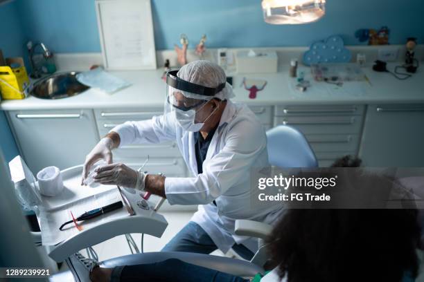 dentist examining teeth of child sitting in dentist chair - face shield stock pictures, royalty-free photos & images