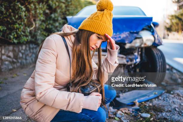 frustrated woman crouches next to wrecked car after a car accident - car accident stock pictures, royalty-free photos & images