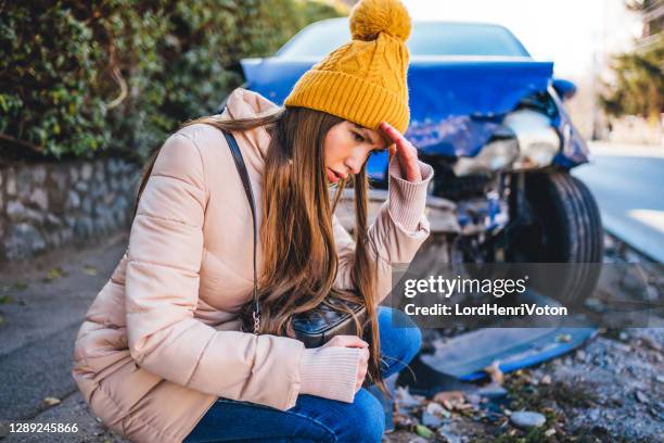 frustrated woman crouches next to wrecked car after a car accident - woman surprised car stock pictures, royalty-free photos & images