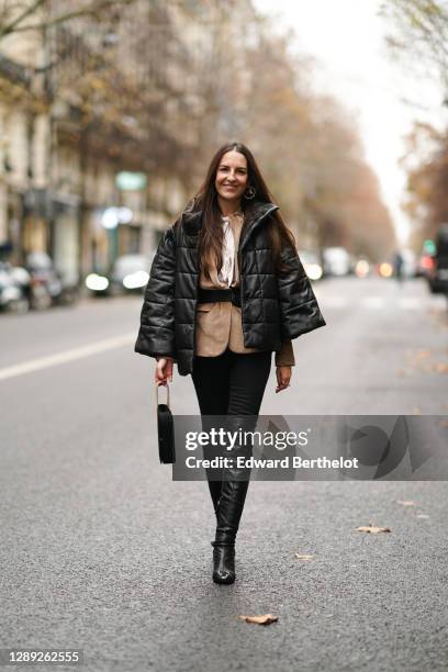 Alba Garavito Torre wears a black oversized winter puffer coat from Munthe, a white shirt, a beige pale brown jacket, a belt, black pants, black...