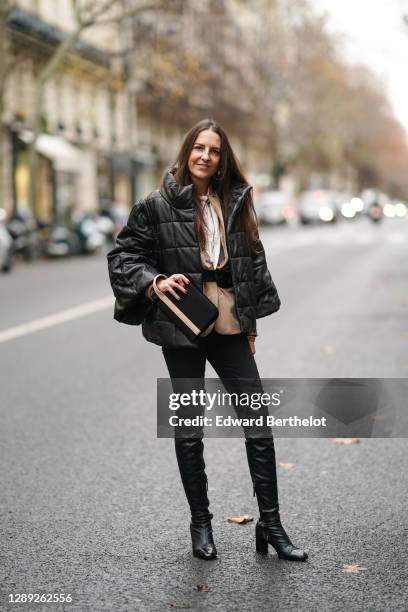 Alba Garavito Torre wears a black oversized winter puffer coat from Munthe, a white shirt, a beige pale brown jacket, a belt, black pants, black...