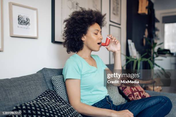 young afro woman using asthma inhaler at home - inhaler stock pictures, royalty-free photos & images