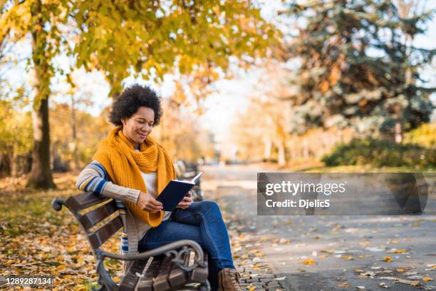 joven afroamericana leyendo un libro en el parque público. - mujer leyendo libro en el parque fotografías e imágenes de stock