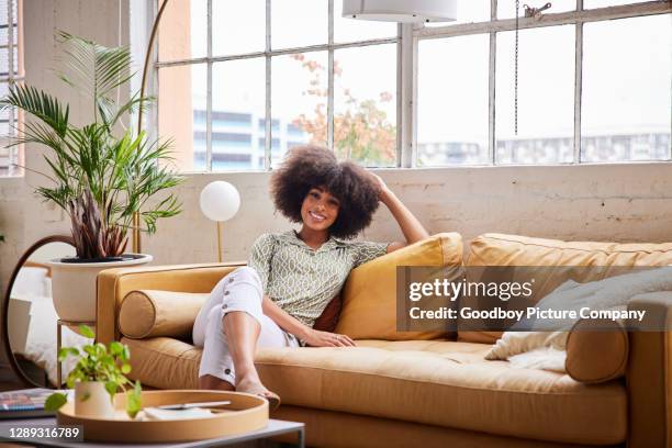 jeune femme de sourire détendant sur un sofa confortable à la maison dans l’après-midi - femme salon photos et images de collection