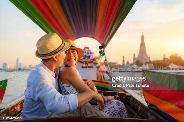 attractive mixed race romantic couple sightseeing wat arun in chao phraya river with longtail boat tour along the river in bangkok, thailand - longtailboot stockfoto's en -beelden