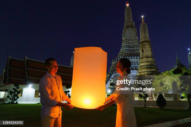 mixed race romantic lover couple in wat arun in night time and floating lamp in yi peng festival under loy krathong day, bangkok city ,thailand - night and day festival stockfoto's en -beelden