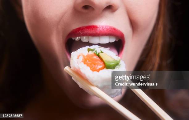 young woman mouth eating sushi piece on chopsticks - japanese food stock pictures, royalty-free photos & images