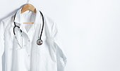 Doctor's white coat with stethoscope on hanger over white background with copy space.
