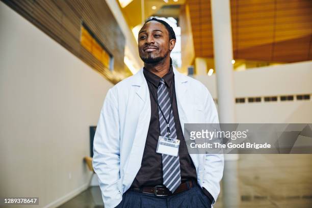 confident doctor with hands in pockets standing in hospital lobby - candid stock pictures, royalty-free photos & images