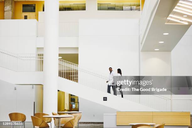 doctors walking up staircase in hospital lobby - medizinische einrichtung stock-fotos und bilder