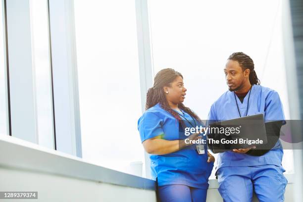 female nurse talking to male colleague with laptop against window in hospital - nurse talking stock pictures, royalty-free photos & images