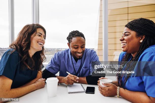 cheerful male and female nurses talking at table in hospital - nurse talking stock pictures, royalty-free photos & images