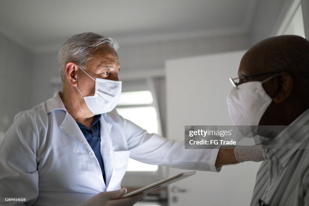 Doctor using digital tablet consoling senior patient in a hospital - using face mask
