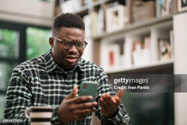 junger afroamerikanischer mann mit schlechten nachrichten auf seinem smartphone lesen - frustration stock-fotos und bilder