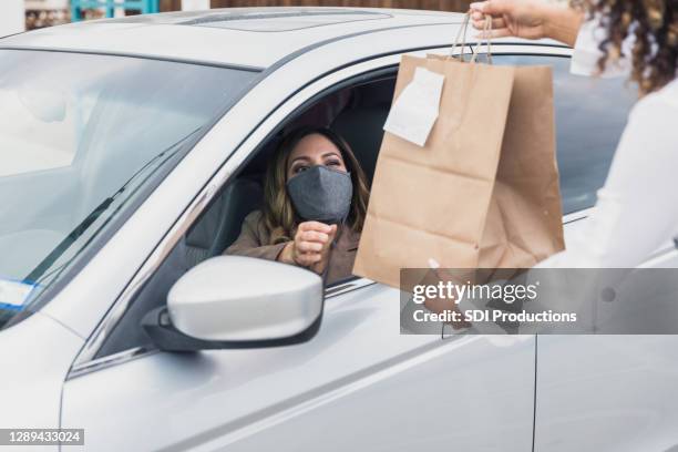 woman with protective mask drives up to get curbside order - drive through stock pictures, royalty-free photos & images