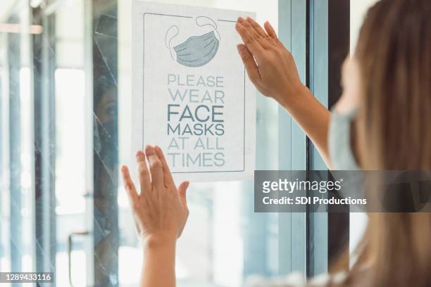 de vrouw plaatst informatiebord op deur tijdens covid-19 - flyers business people stockfoto's en -beelden