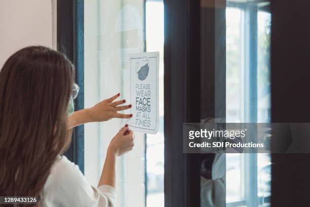 de onderneemster plaatst gezicht masker eisteken op de deur van het kantoorgebouw - flyers business people stockfoto's en -beelden