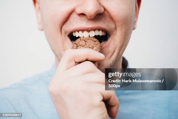 close-up of man biting chocolate cookie against white background,new york,united states,usa - mordere foto e immagini stock