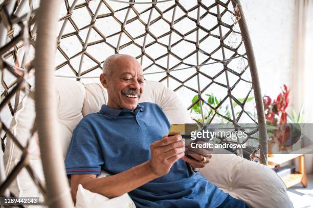 adult senior man using mobile phone and holding credit card in hand in the living room at home - seniors shopping stock pictures, royalty-free photos & images