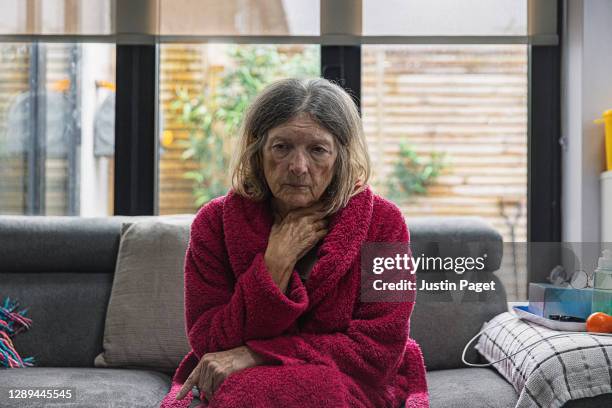 sad senior woman sitting on sofa - vulnerability stock-fotos und bilder