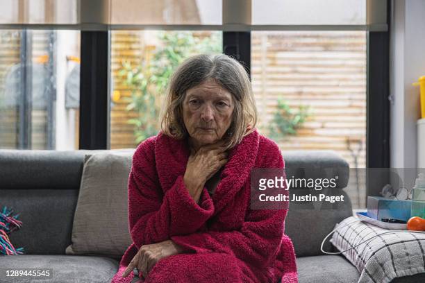 sad senior woman sitting on sofa - vulnerable species stock photos et images de collection