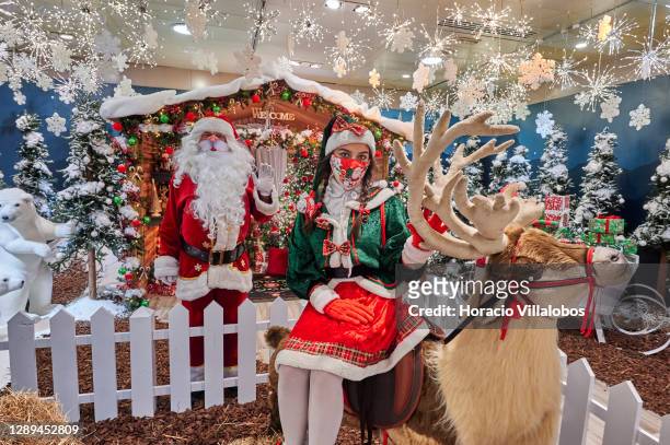 Santa Claus and an elf wear mandatory protective masks in the Christmas setting of Corte Ingles department store during the COVID-19 Coronavirus...