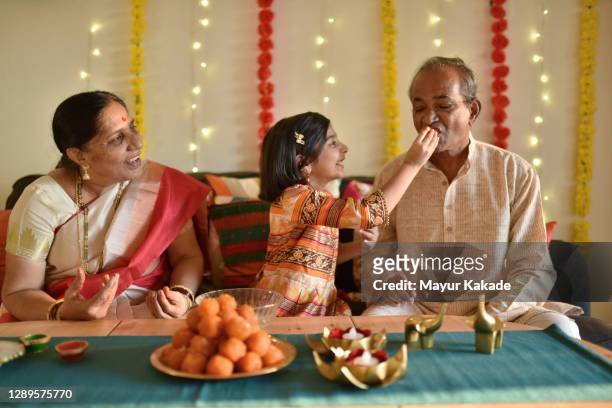 girl enjoying snacks with grandparents during diwali celebration - diwali celebration fotografías e imágenes de stock