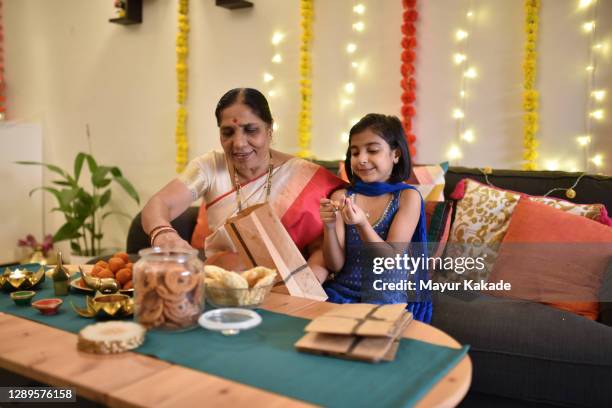 grandmother packing a diwali snacks gift bags and granddaughter eating - diwali celebration fotografías e imágenes de stock