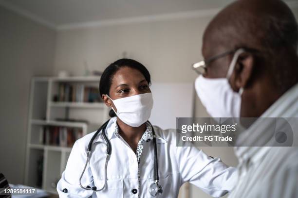 mujer médico consolando al paciente mayor durante la cita médica - usando mascarilla facial - old man afro fotografías e imágenes de stock