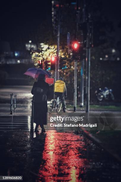 woman with rain umbrella with red traffic light at the pedestrian crossing, at night in the center of milan - couple crossing street stock pictures, royalty-free photos & images