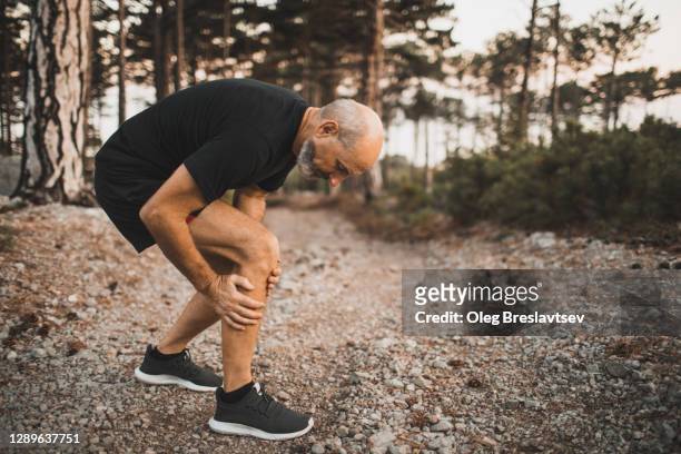 knee injury on running outdoors in forest. senior man holding knee by hands and suffering with pain. sprain ligament or meniscus problem. - calf human leg stock pictures, royalty-free photos & images