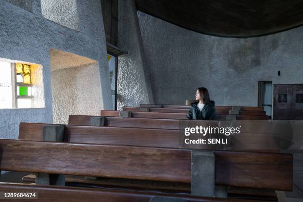 an asian woman sitting on a bench in a french church looking at the window - chinese house churches stock pictures, royalty-free photos & images
