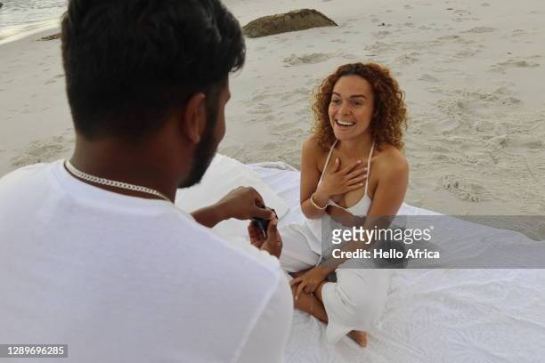 an ecstatic beautiful young woman expressing breathlessness whilst being proposed to with a ring on the beach - black women engagement rings imagens e fotografias de stock