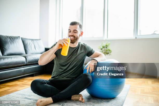 fit man drinking juice and resting after intensive home workout - fitness ball imagens e fotografias de stock