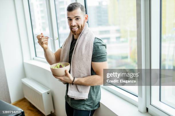 young man eating fresh salad after intensive home workout - sportsman imagens e fotografias de stock