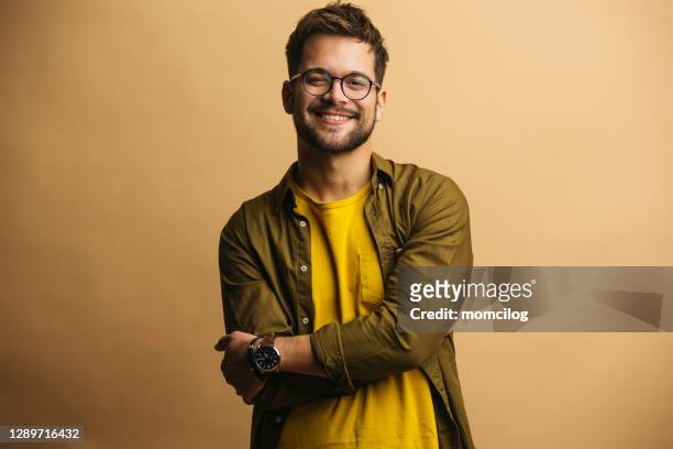 joven adulto seguro de hombre de pie y sonriendo - guay fotografías e imágenes de stock