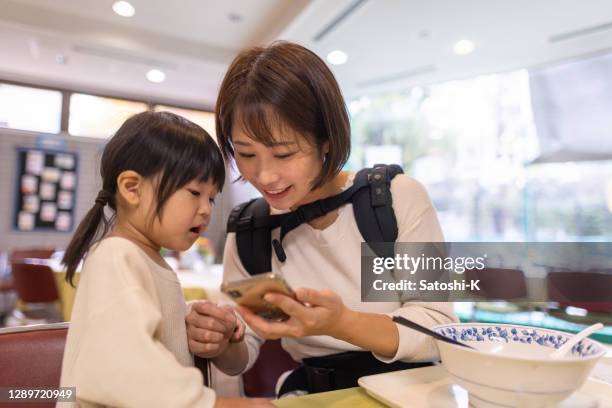 一緒にスマートフォンの画面を見て若い母親と彼女の娘 - スマホ レストラン ストックフォトと画像