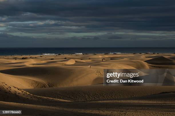 People walk through the sand dunes at sunset on December 05, 2020 in Maspalomas, Spain. The dunes at Maspalomas have seen a positive transformation...