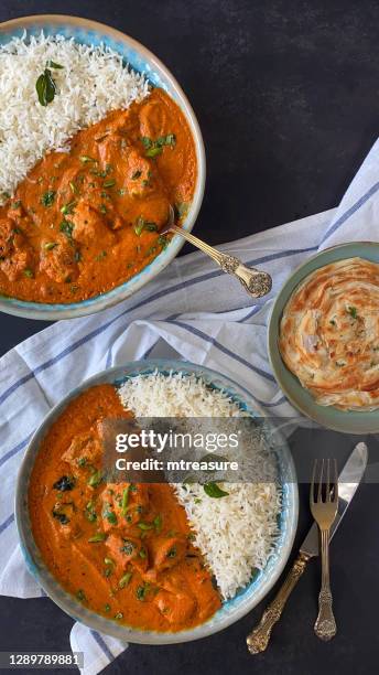 bild von blauen tellern gefüllt mit butter huhn / tikka curry, große stücke von hähnchenbrustfleisch in currysauce mit garnierung von roten zwiebelscheiben und senfsamen mit weißem reis, lachha paratha (geschichtetes fladenbrot), schwarzer hintergrund - parantha stock-fotos und bilder