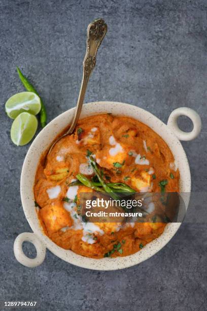image of kadhai-style serving bowl filled with homemade shahi paneer (cheese curry), thick gravy, cream, tomatoes, indian spices with metal spoon, grey background, elevated view - panir stock pictures, royalty-free photos & images