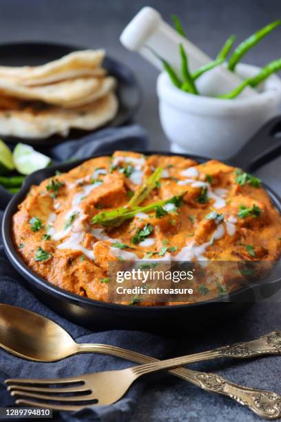 close-up image of cooking pan of homemade shahi paneer (cheese curry) on grey cheesecloth, thick gravy, cream, tomatoes, indian spices served with lachha paratha (layered flatbread), cutlery, bowl of raita, chutney, mortar and pestle, focus on foreground - mortar and pestle stock pictures, royalty-free photos & images