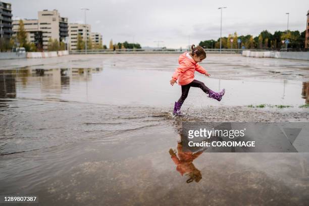 little girl running on a ground wet from rain on cloudy day - purple boot stock pictures, royalty-free photos & images