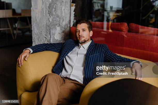 schöne elegante geschäftsmann sitzen in einem gelben sessel - gelber anzug stock-fotos und bilder