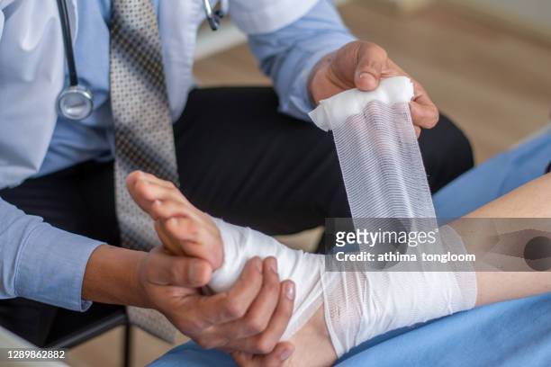 close-up of male doctor bandaging foot of patient at doctor's office. - male feet fotografías e imágenes de stock