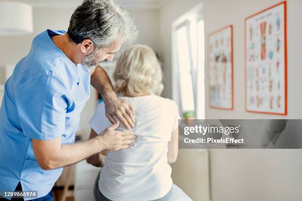 physiotherapist examining a senior patient with back pain - osteopath stock pictures, royalty-free photos & images