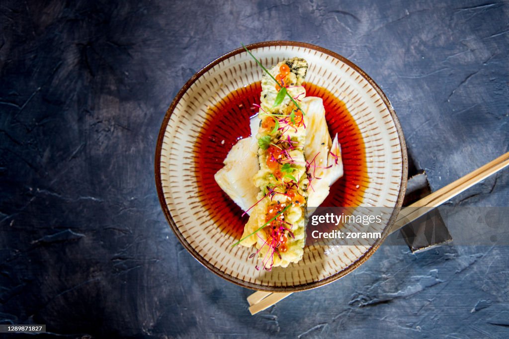 Directly above sea bass fillet with tempura stick on top in soy sauce